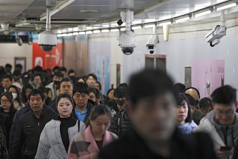 Viajeros caminan junto a las cámaras de vigilancia instaladas en una pasarela entre dos estaciones de metro en Beijing. AP